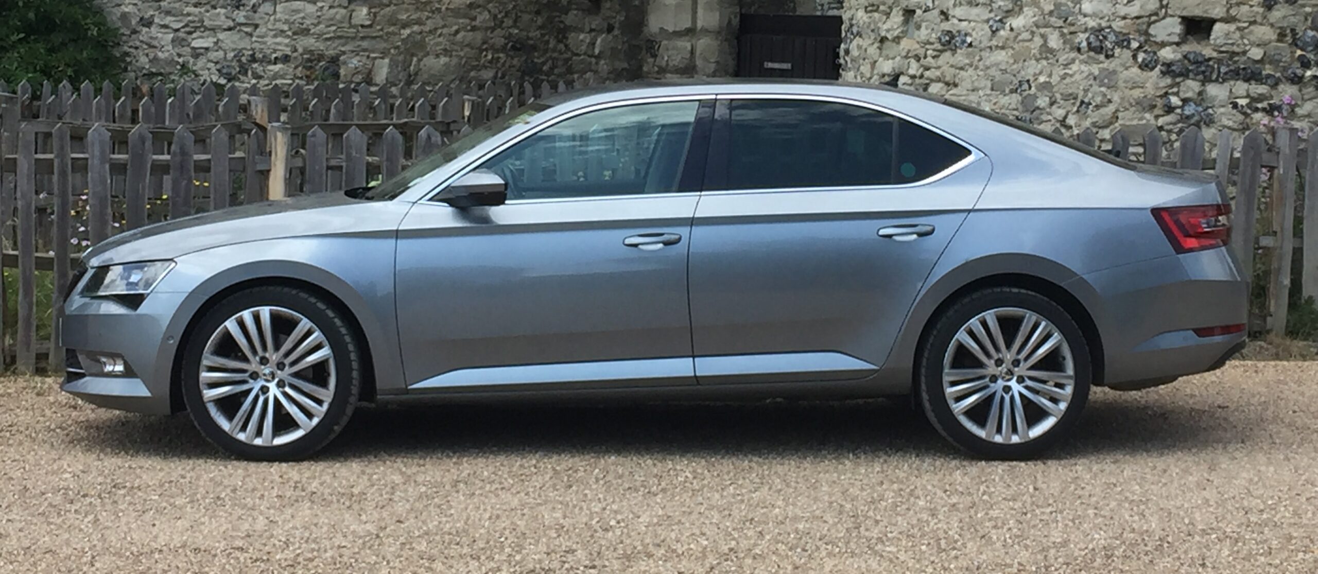 Silver United Cars Skoda saloon parked beside a stone wall
